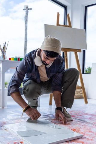 Male artist applying gesso with palette knife on canvas in bright studio workspace