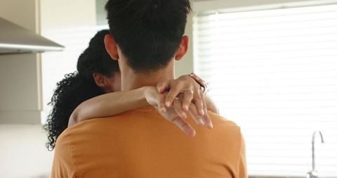 Asian man embracing african american woman in bright kitchen showing rings, warmth and affection