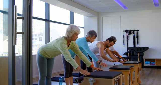 Group of seniors participating in a fitness class in a modern studio with large windows. This image can be used for promoting senior wellness programs, health and fitness services targeted at older adults, or articles about healthy aging and the benefits of regular exercise. Perfect for illustrating community activities and teamwork in promoting an active lifestyle among senior citizens.