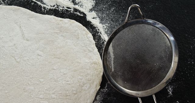 Flour dusting dough alongside sieve for baking preparation. Ideal for illustrating home-baking processes, recipe blogs, food photography, culinary tutorials, or advertising kitchenware.