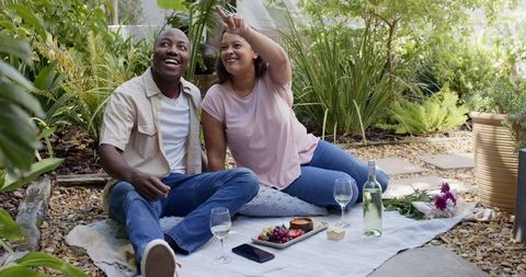 Diverse Couple Enjoying Relaxing Picnic in Garden With Wine and Snacks