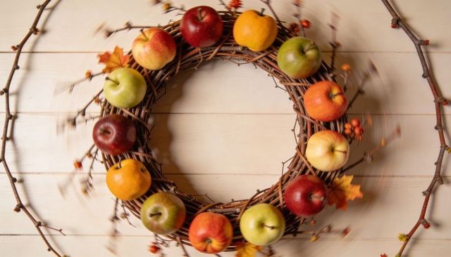 Rustic grapevine wreath with apples and berries on light wood flatlay, autumn centerpiece