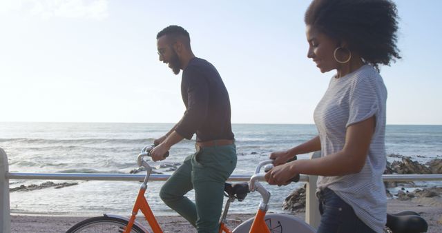 Romantic diverse couple riding bikes and smiling on sunny beach, copy space. Summer, vacation, transport, hobby, romance, love, relationship, free time and lifestyle, unaltered.