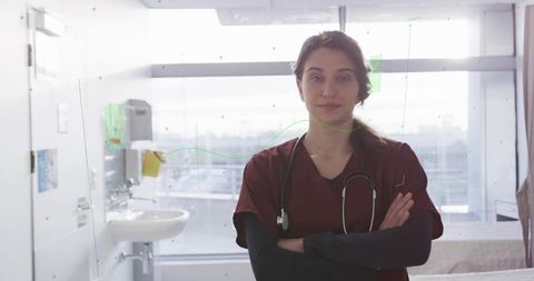 Confident female clinician standing with arms crossed in clinic wearing maroon scrubs