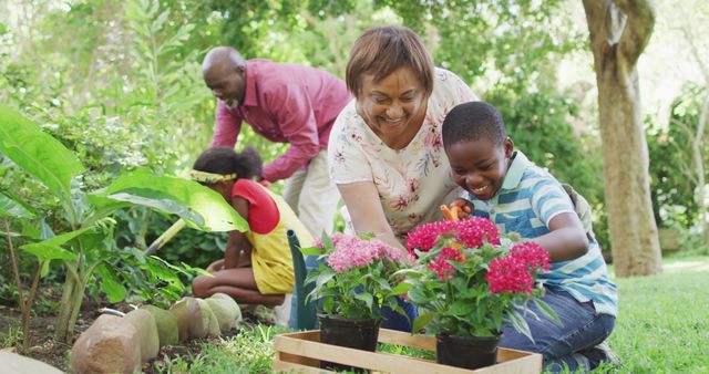 Image of happy african american grandmother and grandson planting flowers in garden. family, gardening, spending quality time together outdoors.