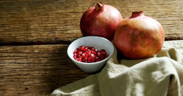 Fresh and whole pomegranates sitting alongside a bowl of their vibrant seeds placed on a rustic wooden table. This imagery exudes a natural, farm-to-table feel, ideal for promoting health and wellness content, food blogs, nutritional guides, and culinary crafts. Perfect for advertising fresh produce, organic products, and fruit-based recipes.