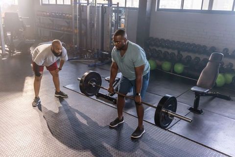 African man deadlifting under trainer supervision in gym — strength training session
