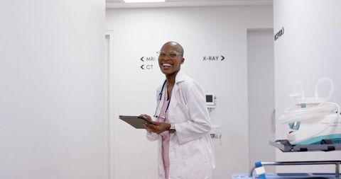 Smiling african female doctor using tablet in radiology corridor with mri ct x-ray signs