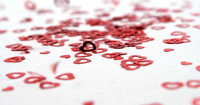 Red heart-shaped confetti scattered on a white surface, suitable for Valentine's Day themes, romantic celebrations, and festive decorations. Perfect for designs, cards, and social media posts centered around love and romance.