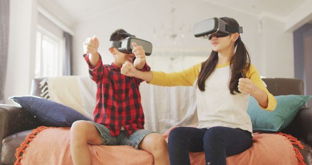 Children experiencing virtual reality while playing games at home. They are wearing VR headsets and appear to be having a great time, making the image suitable for themes of family fun, modern technology, indoor activities, and entertainment. This can be used in campaigns promoting tech gadgets for kids, family-oriented technology products, or articles about the impact of VR in children's entertainment.