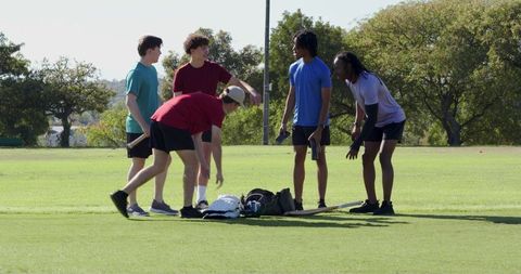 Diverse young men unloading athletic gear, huddling and taking group selfie on green field