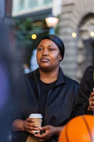 African american woman standing and holding coffee near basketball on urban evening street