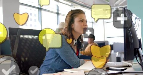 Engaged young woman working on computer in bright open office with social reaction icons