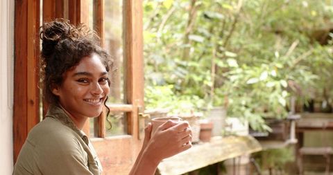 Smiling Woman Relaxing with Coffee on Veranda amidst Greenery