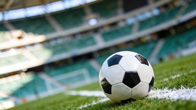 Sitting classic soccer ball on white sideline of stadium pitch with goal and stands