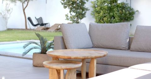 Minimal neutral patio living with light gray sofa, round wooden tables and poolside calm