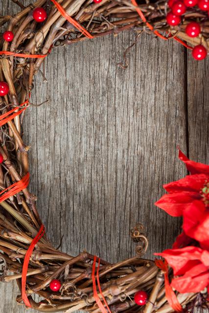 Close-up of a grapevine wreath adorned with red berries and a poinsettia flower on a rustic wooden plank. Ideal for use in holiday-themed promotions, Christmas decorations, seasonal greeting cards, or DIY craft tutorials.