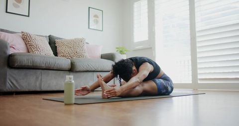 African american woman stretching on yoga mat in sunlit living room for home wellness