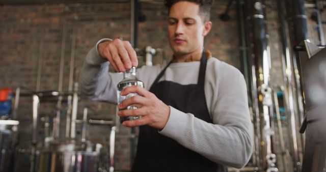 Young bartender shaking a cocktail in an industrial-style bar. Ideal for use in advertisements promoting bars, night clubs, or alcoholic beverages. Suitable for articles on mixology, cocktail recipes, or bartender skills.