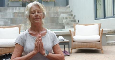 Senior woman meditating on patio wearing headphones and smartwatch for mindful wellness