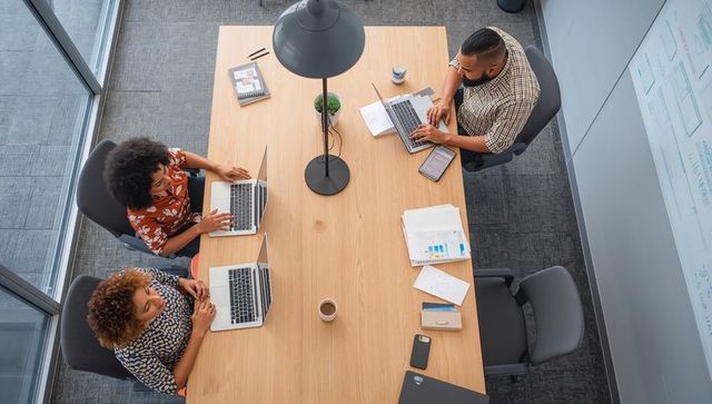 Overhead view of diverse team collaborating at modern wooden table with laptops and charts