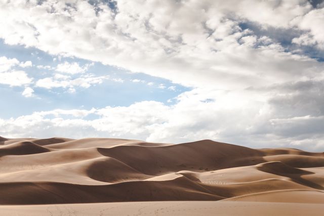 Expansive sand dunes with soft curves under a mostly cloudy sky. The scenery highlights natural patterns and interplay of light and shadow. Useful for illustrating concepts of solitude, tranquility, arid environments, and natural beauty. Ideal for travel websites, nature photography collections, and backgrounds emphasizing vast outdoor spaces.