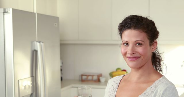 Smiling Woman with Curly Hair Holding Glass of Water in Modern Kitchen - Download Free Stock Images Pikwizard.com