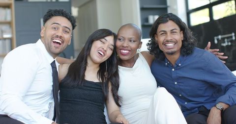 Multicultural friends laughing on sofa in bright modern living room celebrating together