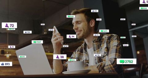Young man using smartphone and laptop in cafe with social media notifications