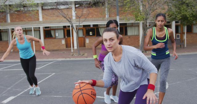 Diverse female basketball team playing match, dribbling ball. basketball, sports training at an outdoor urban court.