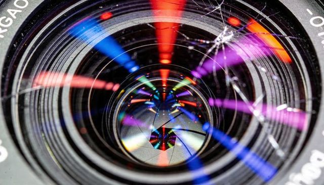 Macro cracked camera lens reflecting colorful light streaks with visible aperture blades