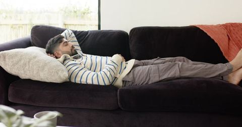 Indian man lounging on dark velvet sofa wearing striped sweater, relaxed home interior