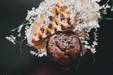 Tasty chocolate muffin amongst delicate flowers and cookie