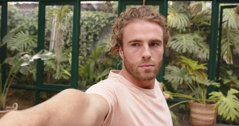 Man Practicing Yoga in Glasshouse Surrounded by Lush Greenery