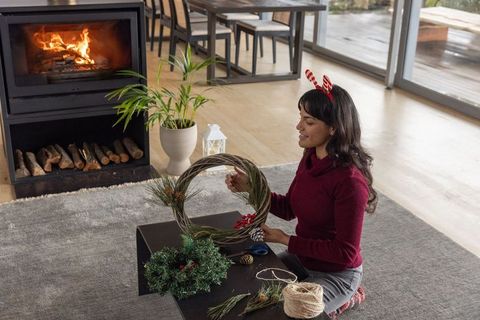 Asian woman creating craft wreath in cozy modern living room