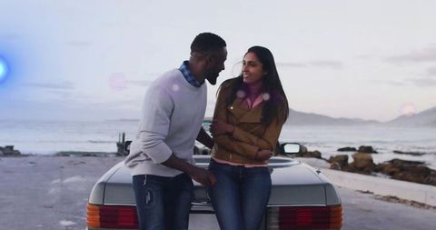 Couple leaning and sitting on convertible trunk by seaside road at sunset cinematic mood