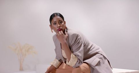 Elegant woman in taupe blazer sitting in minimalist studio