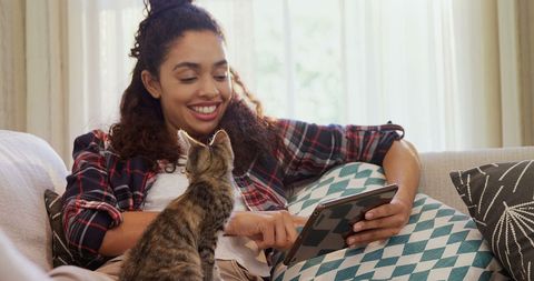 Young woman relaxing at home with cat using tablet