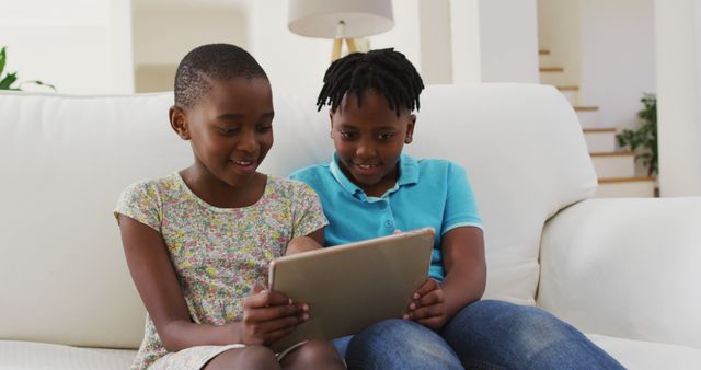 African american boy and girl using digital tablet while sitting on the couch at home. family, togetherness and happiness concept