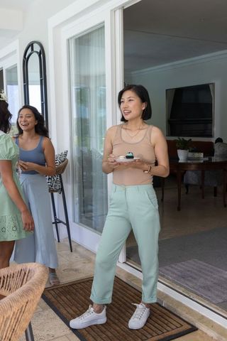 Women enjoying casual indoor-outdoor gathering by sliding door holding teal dessert