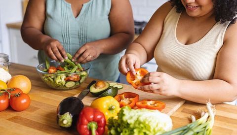 Two women preparing fresh vegetable salad together on wooden counter with colorful produce