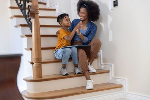 African american mother and hispanic son bonding while using tablet on wooden stairs