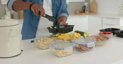 African american man meal-prepping healthy lunches in modern kitchen using black trays