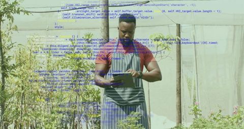 Greenhouse worker tapping tablet while monitoring plant growth for sustainable farming