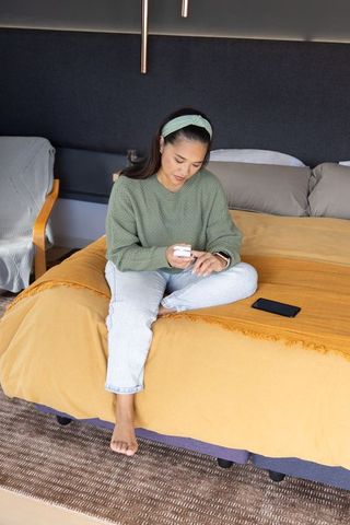 Mid-adult asian woman sitting on bed checking blood glucose with handheld meter