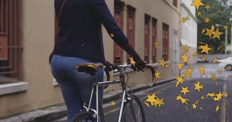 Woman walking bicycle down cozy street with floating gold stars