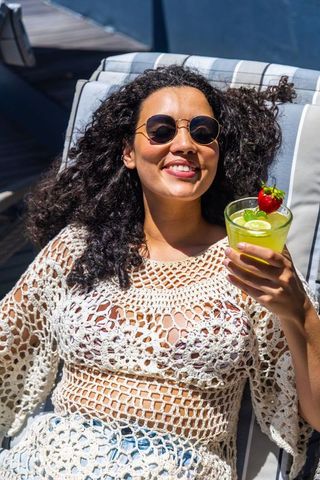Sunlit poolside woman reclining in crochet cover-up holding refreshing citrus cocktail