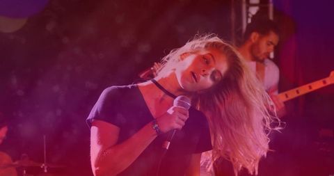 Blonde lead vocalist performing with microphone under red haze lighting at club gig