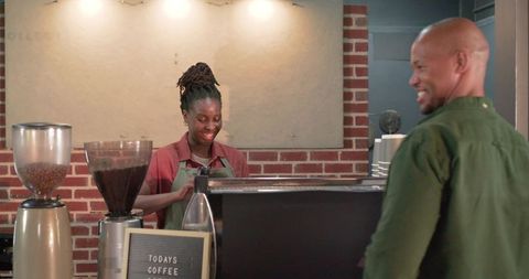 Smiling african american barista serving espresso to customer at brick wall cafe counter