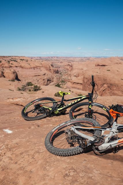 Two mountain bikes are parked on a rocky desert trail, showcasing an expansive desert landscape and clear blue sky. Ideal for promoting outdoor activities, travel, adventure sports, and nature tourism.